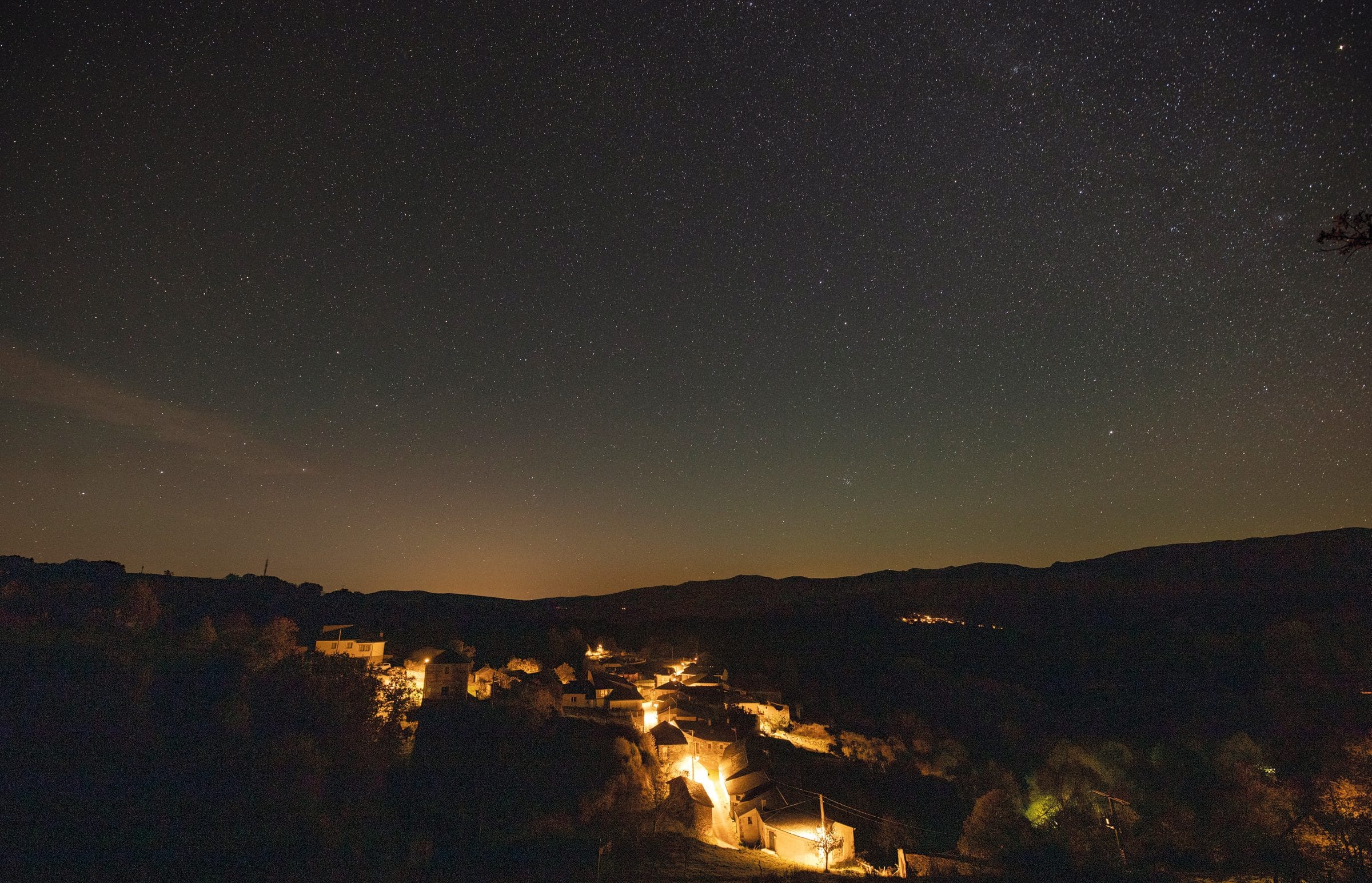 A Veigas de noche: las luces del pueblo brillan en el fondo del valle bajo un cielo despejado.