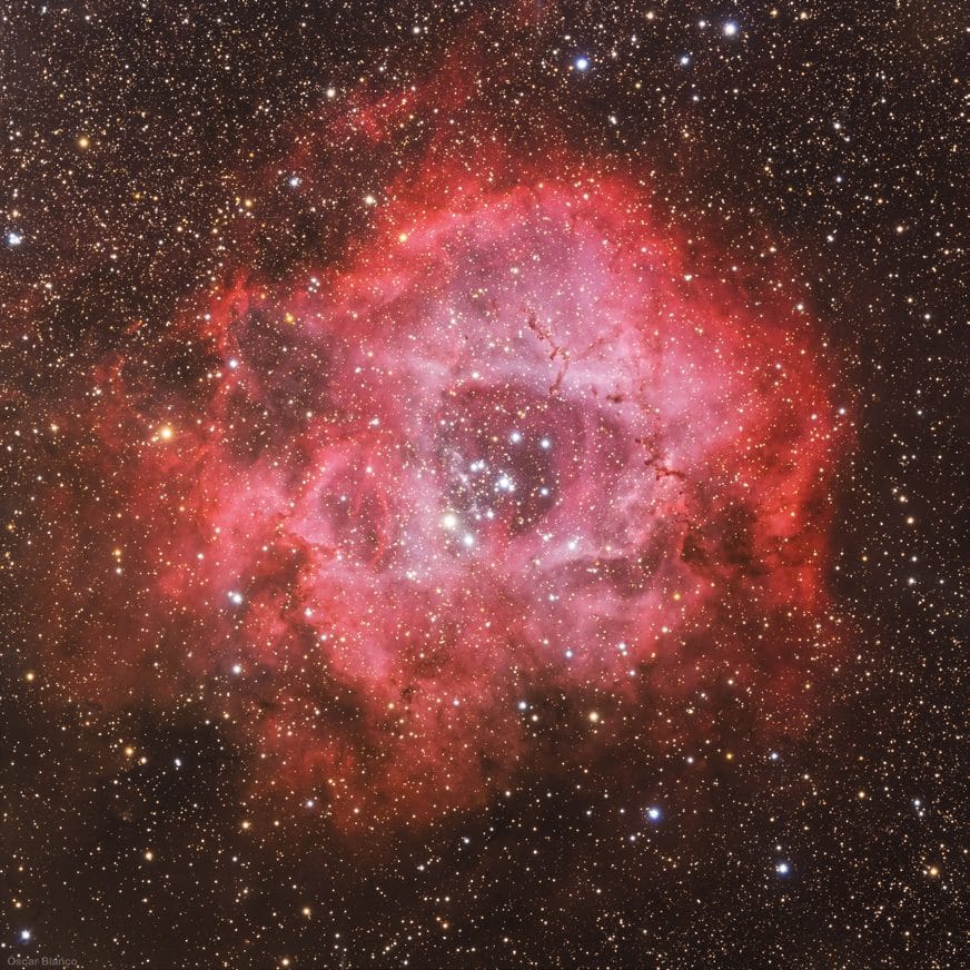 La nebulosa Roseta, un anillo de gas rojo con un cúmulo de estrellas en el centro.