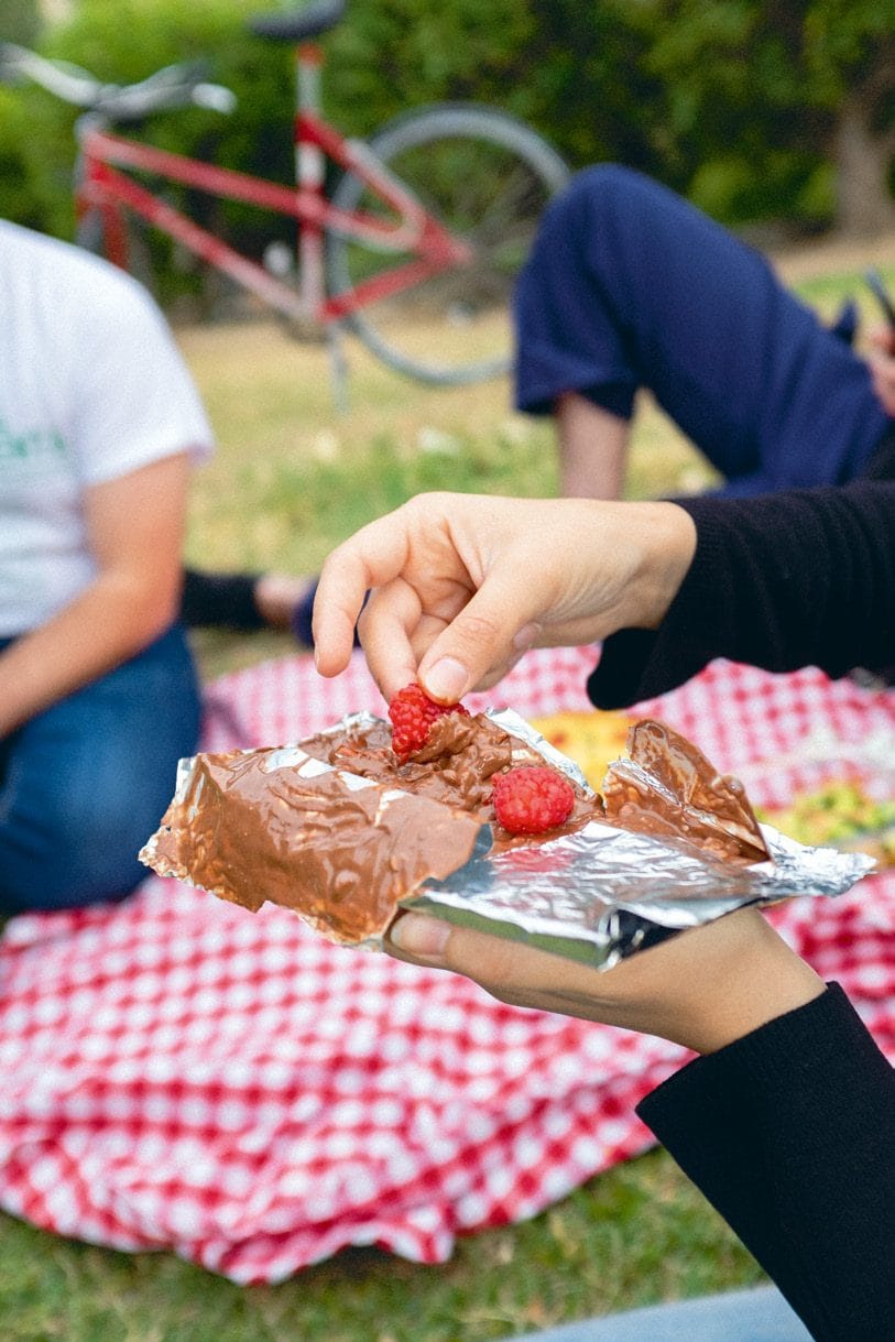 Varias manos cogen fresas y chocolate de una bandeja de aluminio apoyada en el mantel de cuadros.