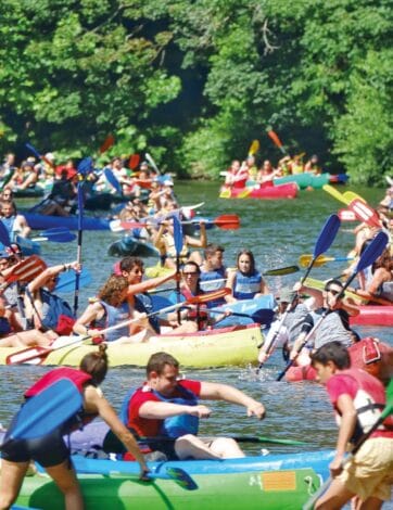 Un tramo de río abarrotado de kayaks de colores con decenas de personas remando muy juntas entre la vegetación de las orillas.