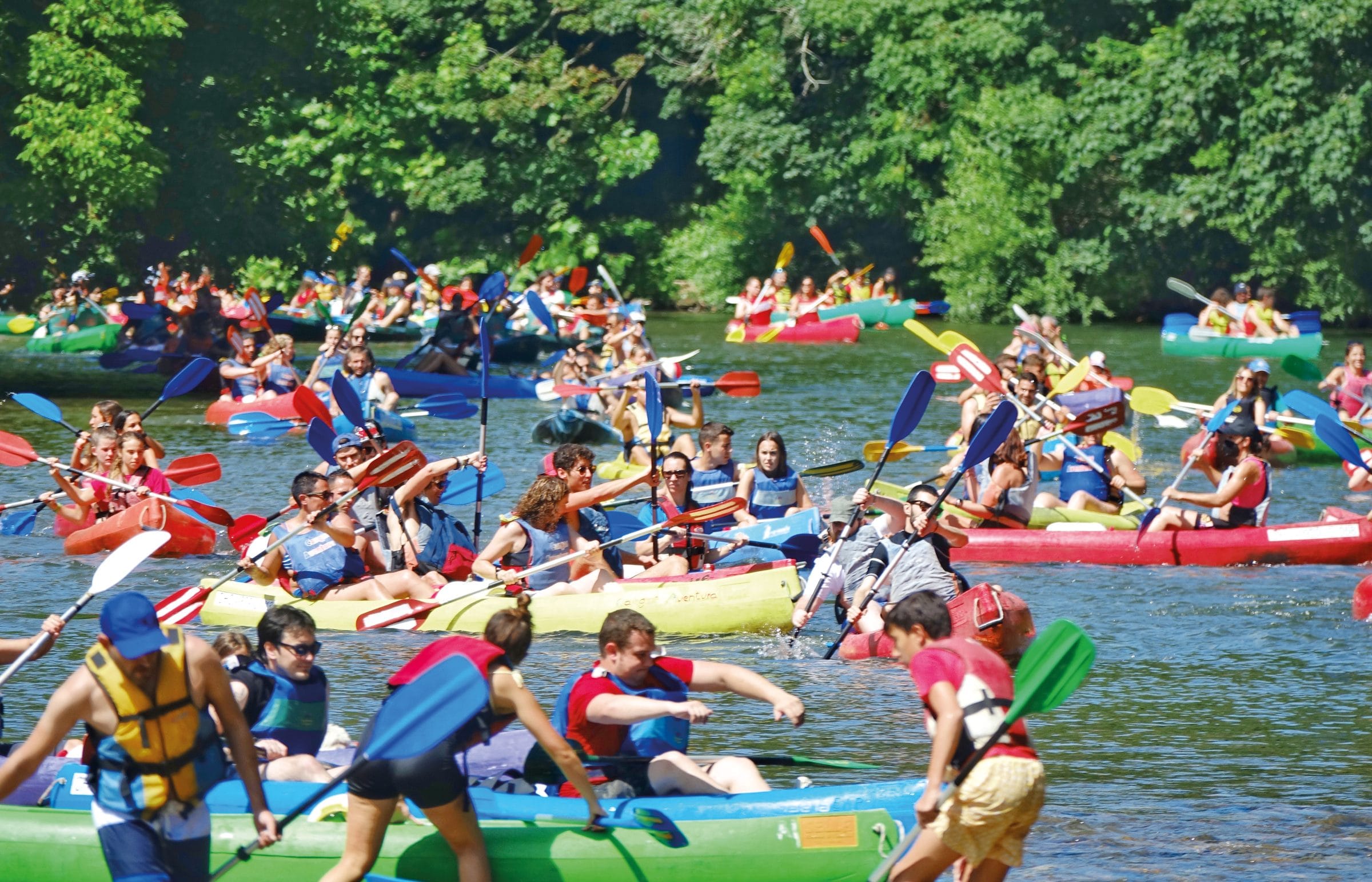 Un tramo de río abarrotado de kayaks de colores con decenas de personas remando muy juntas entre la vegetación de las orillas.