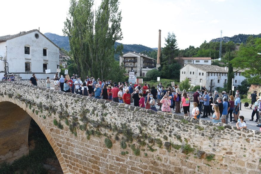 Una multitud cruza en fila un puente de piedra hacia un pueblo.